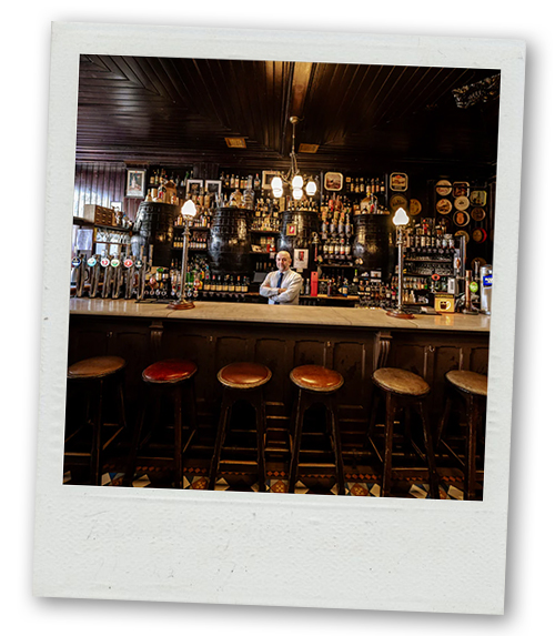 A Polaroid of a bartender stood behind the bar in an old fashioned looking bar