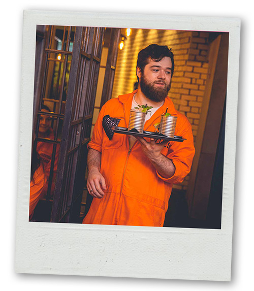 A Polaroid of a man in an orange prison jumpsuit carrying a tray of cocktails