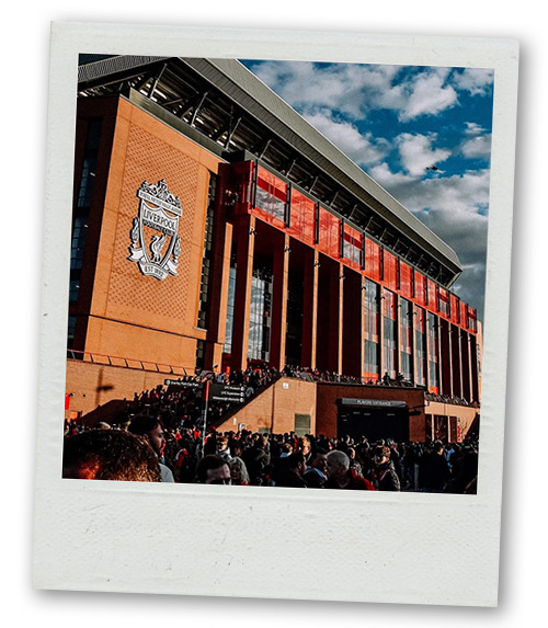 A Polaroid of the outside of Anfield which has a big Liverpool FC crest on it