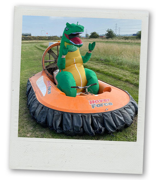 A Polaroid of someone wearing an inflatable dinosaur outfit whilst sitting atop a hovercraft