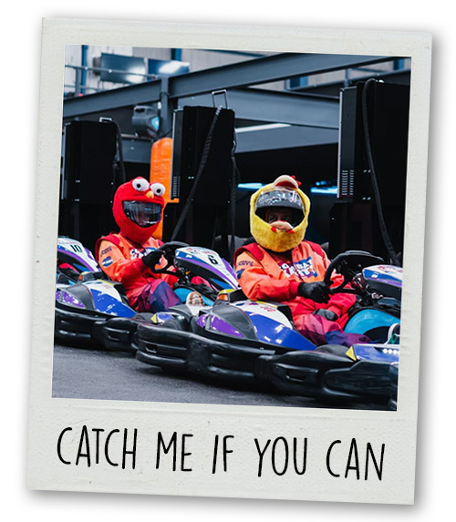 A Polaroid of two men go karting with cartoon looking helmets with the caption Catch Me If You Can