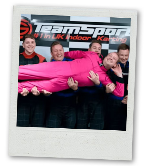 A Polaroid of a man in a pink outfit being held up by a stag do group with the backdrop reading Team Sport