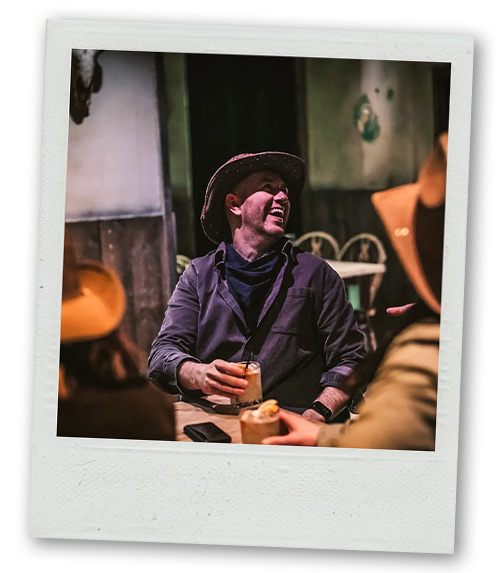 A Polaroid of a man in a cowboy hat drinking a cocktail and laughing