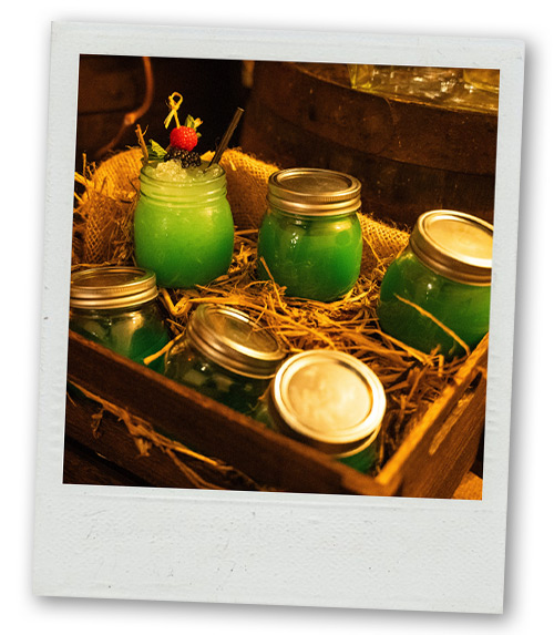 A Polaroid of a bunch of green cocktails sitting in a crate with hay in it