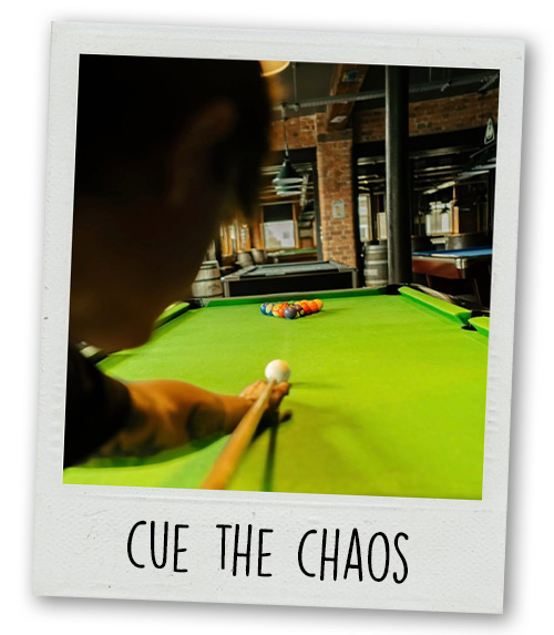 A Polaroid of a man about to do a break shot on the pool table with the caption Cue The Chaos
