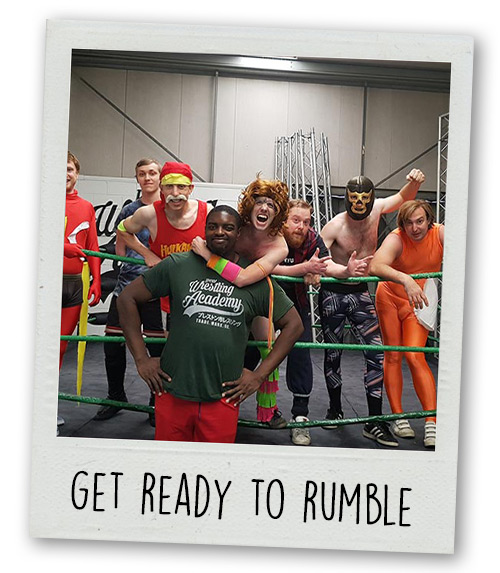 A Polaroid of a stag do group posing in a wrestling ring in wrestling outfits with the caption Get Ready To Rumble