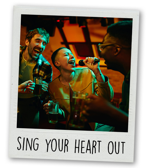 A Polaroid of a small group of people doing karaoke with the caption Sing Your Heart Out