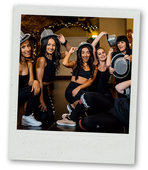 A Polaroid of a hen do group doing a dance class and wearing sparkly silver hats