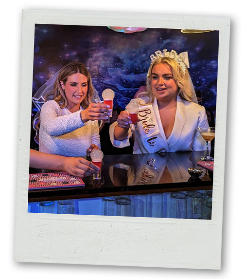 A Polaroid of two women on a hen do drinking fancy looking cocktails