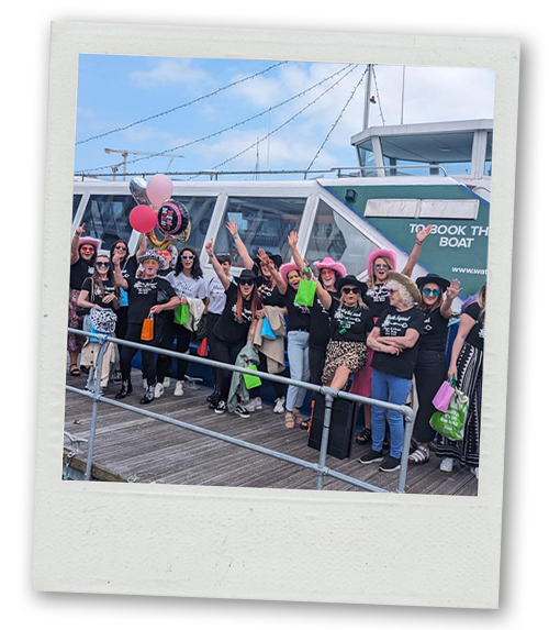 A Polaroid of a hen do group posing in front of a boat about to do a drag cruise
