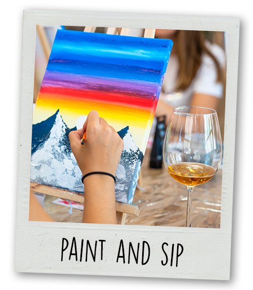 A Polaroid of someone painting a picture of a mountain whilst drinking some wine with the caption paint and sip