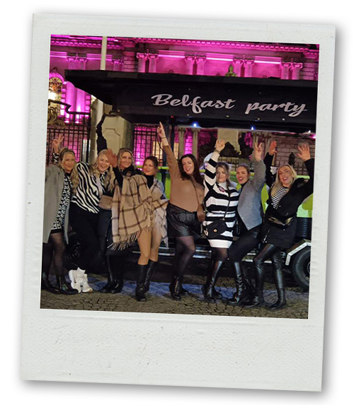 A Polaroid of a hen do group posing in front of the Belfast Pedi Bike that's parked infront of the city hall