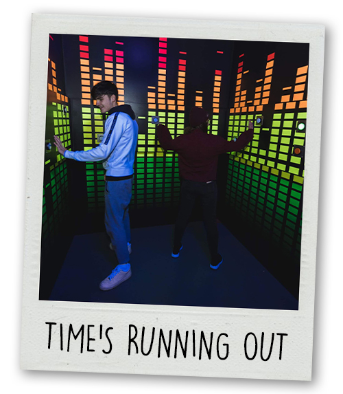 A Polaroid of two men doing a challenge where you have to hit buttons at Prison Island with the caption Time's Running Out