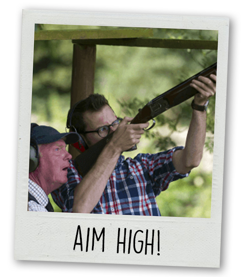 A Polaroid of a clay pigeon shooting instructor teaching a man on a stag do to aim with the caption Aim High