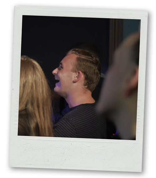 A Polaroid of a man in a crowd at a comedy club laughing