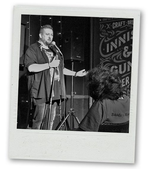 A Polaroid of a man with a beard doing stand up comedy