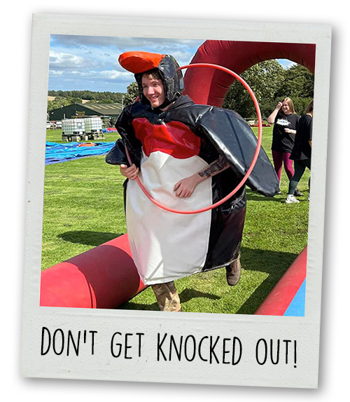 A Polaroid of a man in a penguin outfit running through an inflatable obstacle with the caption Don't Get Knocked Out