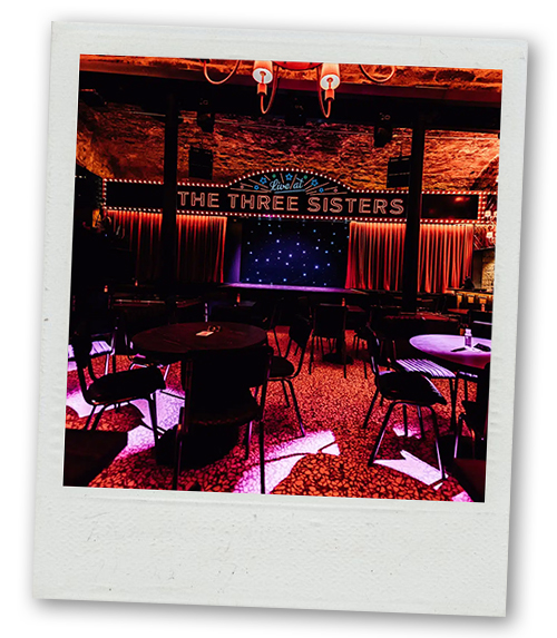A Polaroid of an indoor stage with The Three Sisters above it