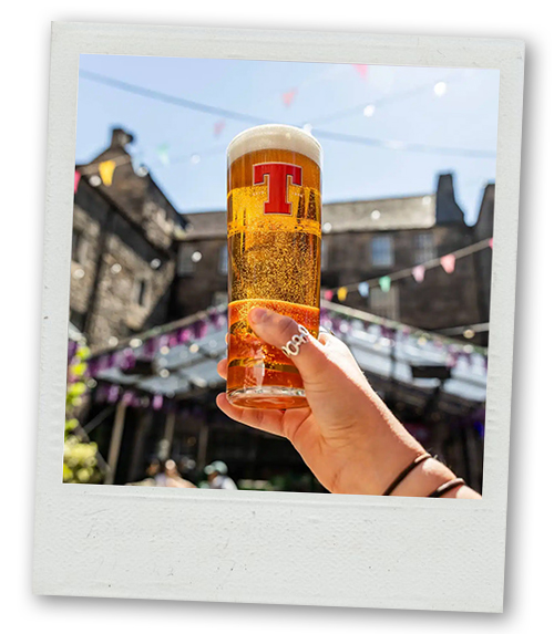 A Polaroid of someone holding up a pint of Tenants with the courtyard of The Three Sisters in the background