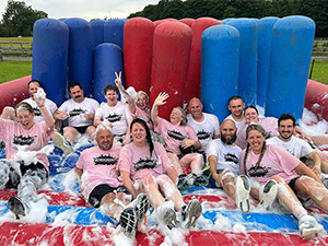 A mixed gender group taking part in It's a Knockout sitting on a soapy inflatable 