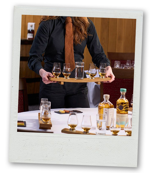 A Polaroid of someone in a smart work uniform holding a tray of whisky