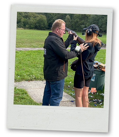 A Polaroid of a male instructor teaching a woman how to do clay pigeon shooting
