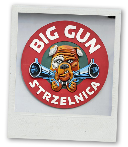A Polaroid of a sign with a bulldog on it that's pointing two pistols that reads Big Gun Strzelnica