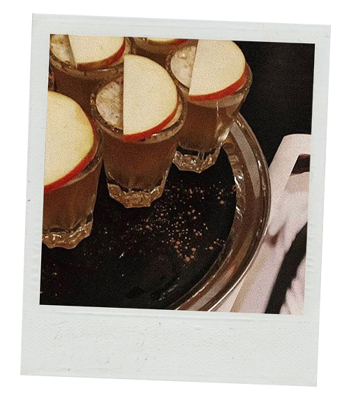 A Polaroid of a tray of vodkas that have apple slices on them