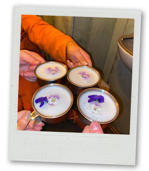 A Polaroid of people clinking cocktails that are white with purple and white flowers on top