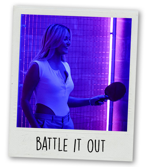 A Polaroid of a woman holding a ping pong paddle with the caption Battle It Out