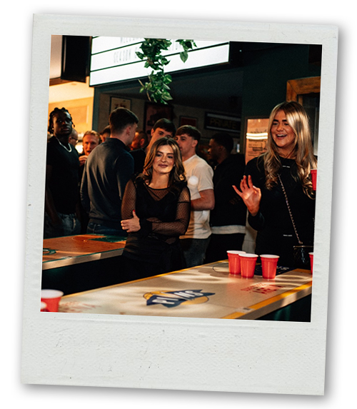 A Polaroid of some women playing beer pong at Pins