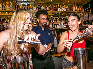 A male bartender showing two women on a hen do how to make a cocktail 