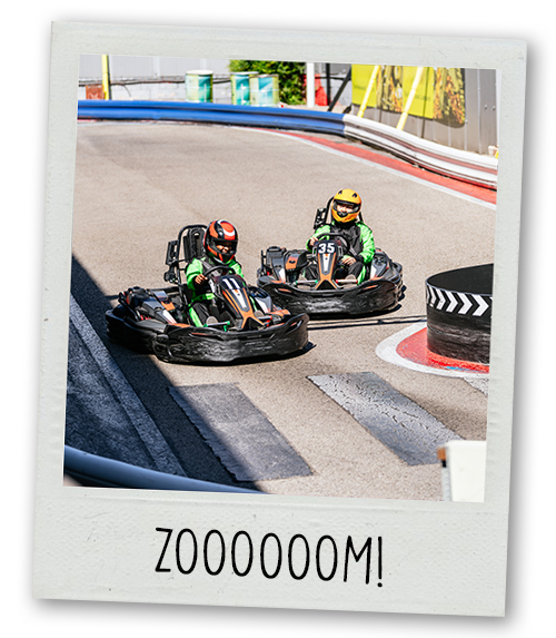 A Polaroid of two people go karting at an outdoor track with the caption Zoooom!