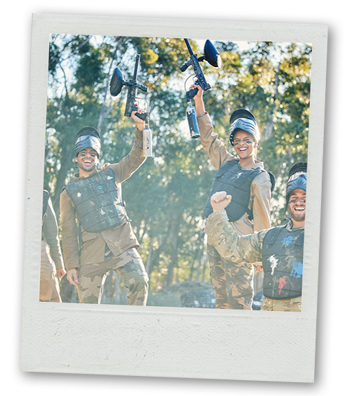 A Polaroid of a mixed gender group holding their paintball guns high in the air