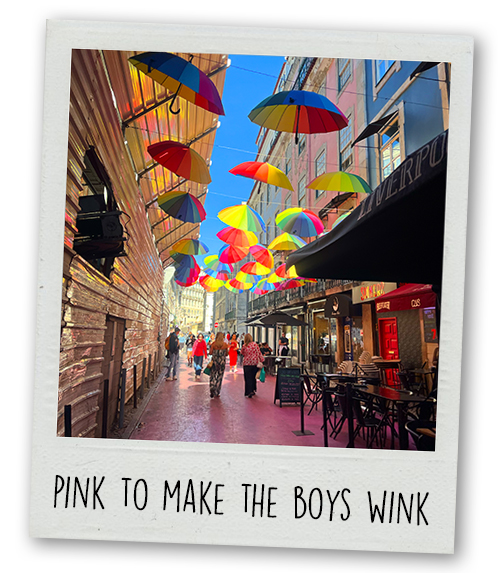 A Polaroid of Pink Street which has a pink floor and umbrellas hanging over the street with the caption Pink to make the boys wink