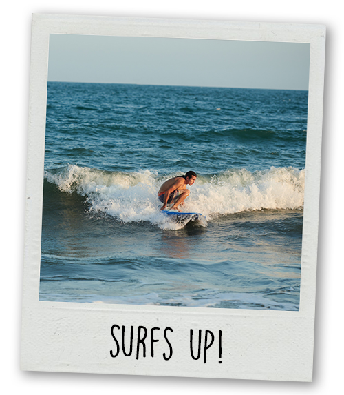 A Polaroid of a man surfing a wave with the caption Surfs Up