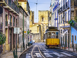 A street in Lisbon that has colourful houses, a tram and a church at the bottom of the street