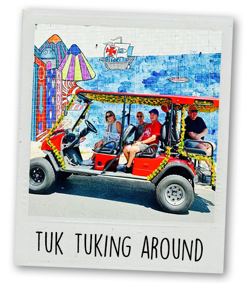 A Polaroid of some people doing a Tuk Tuk tour in front of a colourful wall art background with the caption Tuk Tukking Around