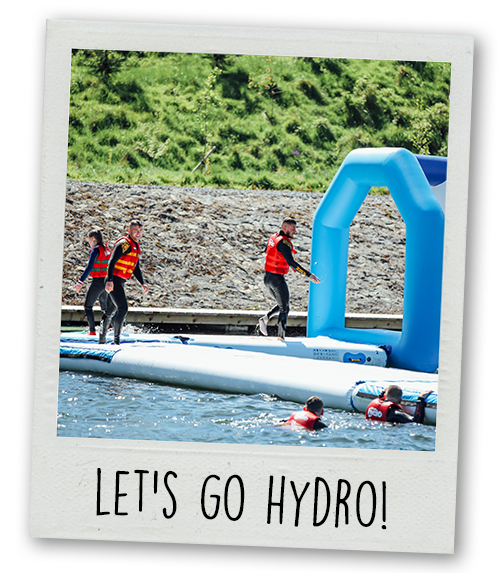 A Polaroid of a group of people doing an inflatable course that is floating on water with the caption Let's Go Hyro!