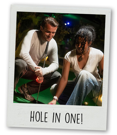 A Polaroid of a man and a woman crouched down next to a hole in mini golf with the caption Hole in One