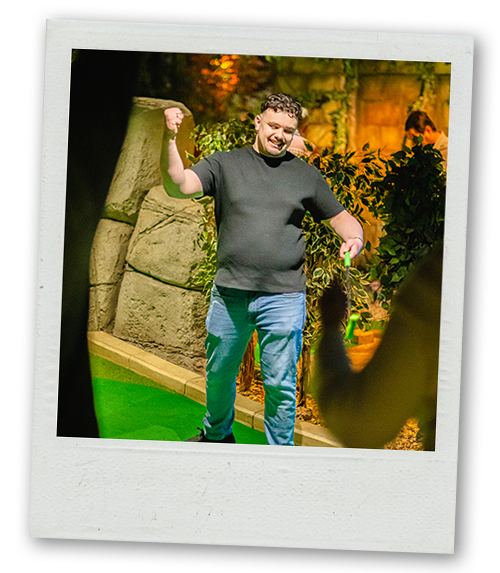 A Polaroid of a man swinging a mini golf club on an aztec themed mini golf course