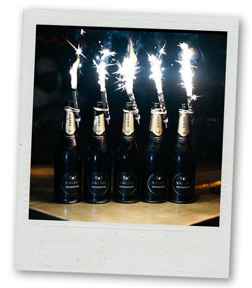 A Polaroid of five bottles of champagne with sparklers in them