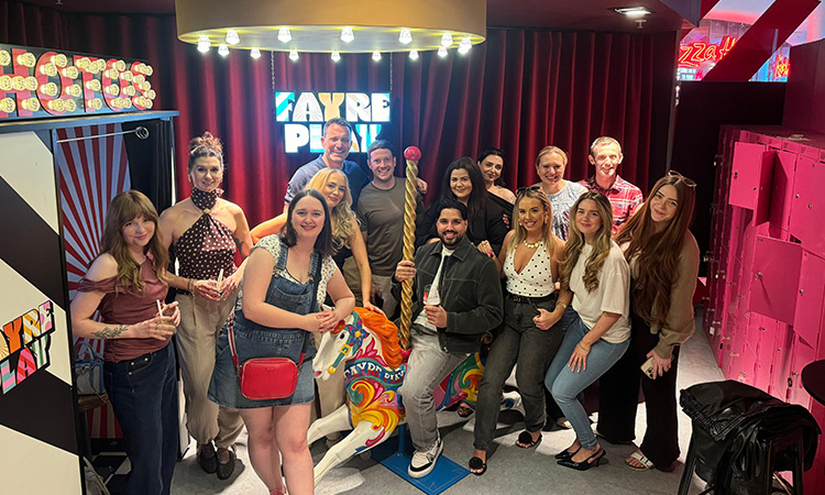 A team pic of Last Night of Freedom staff posing around a carousel horse and a sign reading Fayre Play