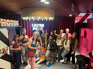 A team pic of Last Night of Freedom staff posing around a carousel horse and a sign reading Fayre Play