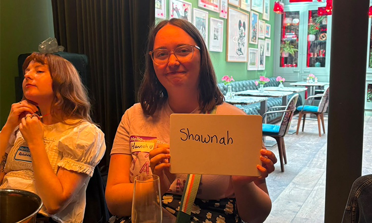 A woman with a brown bob holding up a whiteboard reading Shawnah