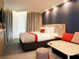 A double bed with orange decor and a sofa next to it at Holiday Inn Express Belfast City