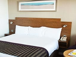 Close up image of a room with a double bed with striped bed runner with a wooden head board 