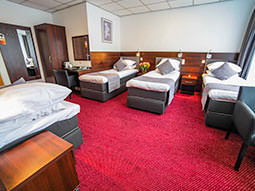 Four single beds in a hotel room, featuring a wardrobe right at the back of the room