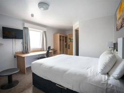 A double bed in a room with a desk area, TV and wardrobe space at Pendulum Hotel