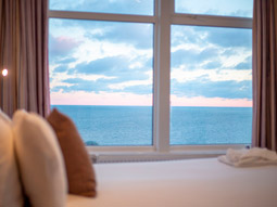 A bed with a window next to it facing the sea at Ocean Beach Hotel